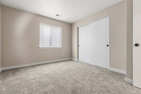 A room with a carpeted floor, a window with blinds, and a white door.