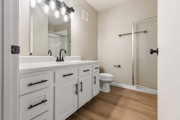 A white bathroom with a sink, mirror, toilet, and a walk-in shower.