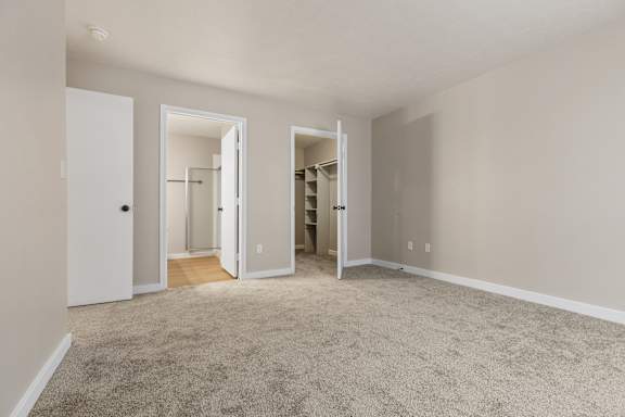 A room with carpeted floor and white walls with three open doors.