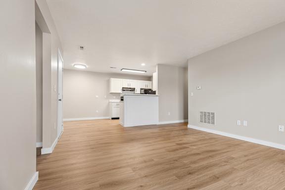 A spacious room with wooden flooring and a kitchen area in the background.