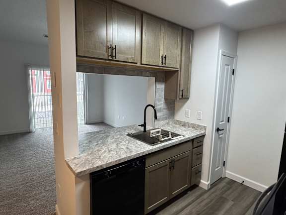 A kitchen with a black dishwasher and a sink under a cabinet.