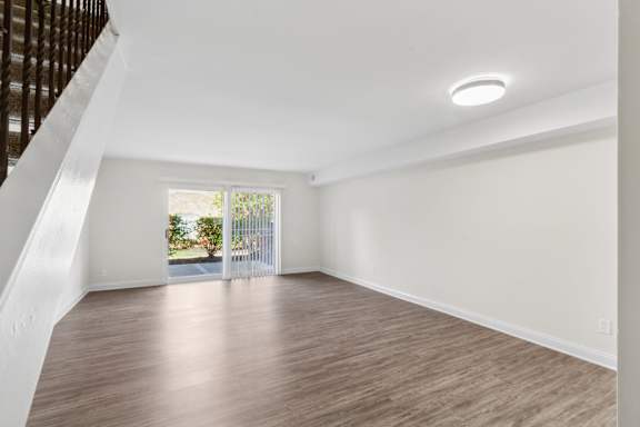 A room with wooden flooring and white walls, with a staircase on the left side.