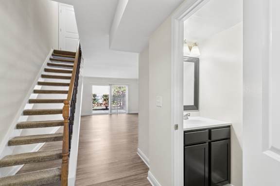 A staircase with a wooden handrail leads to a bathroom with a vanity and a mirror.