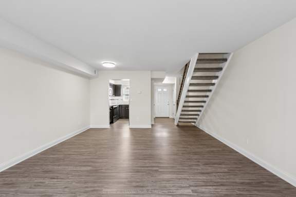 A spacious room with wooden floors and a staircase on the right side.