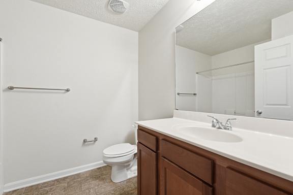 A white toilet sits in a bathroom with a white sink and brown cabinets.
