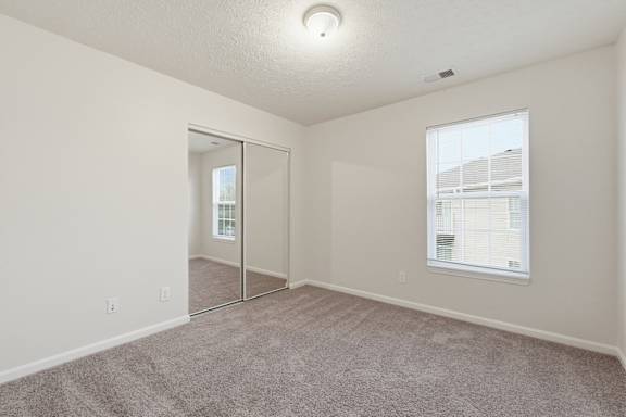 A room with a carpeted floor, a window with blinds, and a sliding glass door.