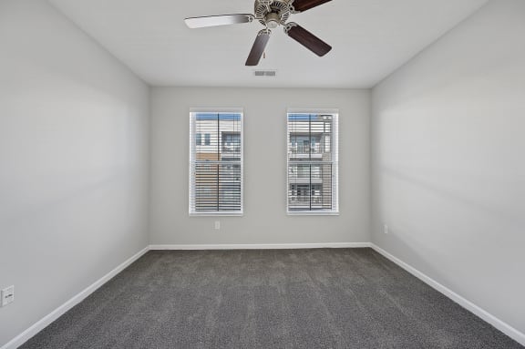 an empty room with a ceiling fan and two windows at Monmouth Row Apartments, Newport