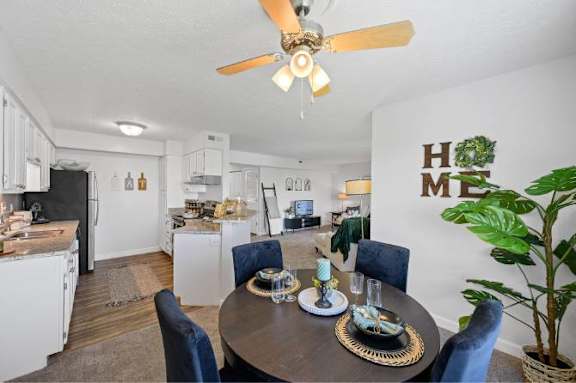 A dining room with a table set for four and a ceiling fan.