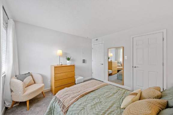 A bedroom with a bed, chair, and nightstand.