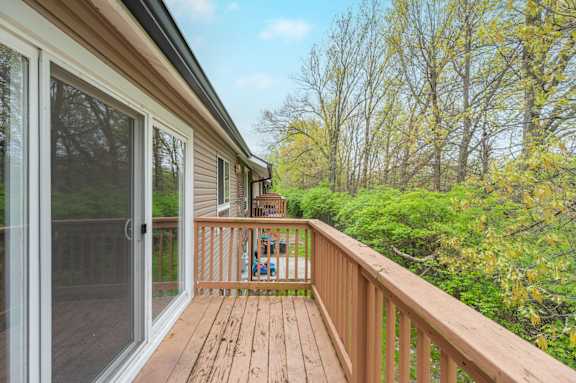 A wooden deck with a sliding glass door leading to a lush green forest.