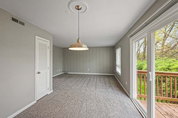 A room with a grey carpet and a hanging light fixture.