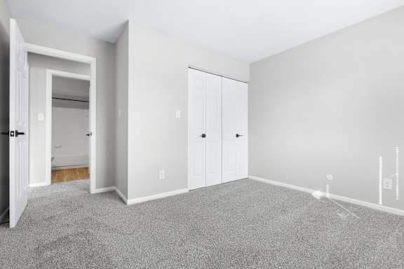 A room with grey carpet and white walls with a doorway leading to another room.