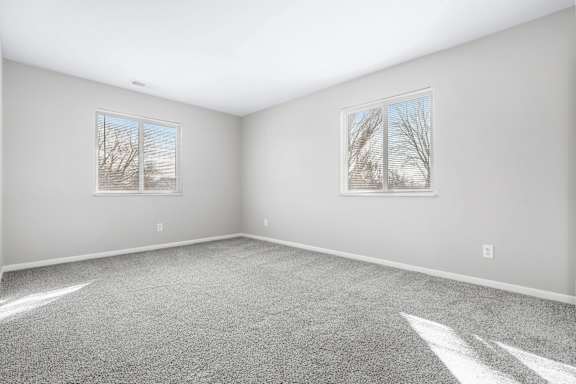 A room with grey carpet and two windows.