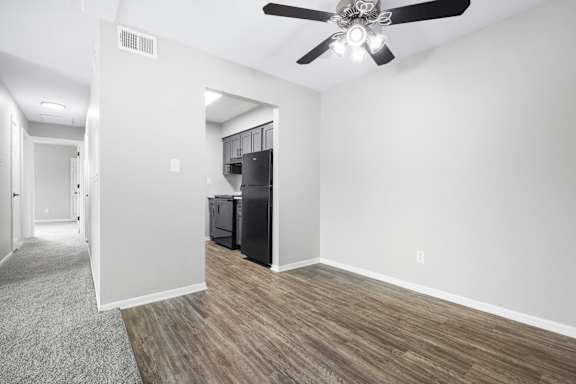 A room with a ceiling fan and a black refrigerator.