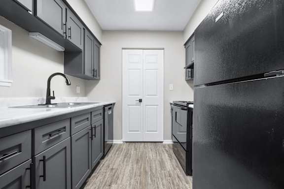 A kitchen with a black refrigerator and wooden floors.