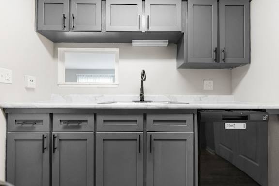 A kitchen with grey cabinets and a white sink.