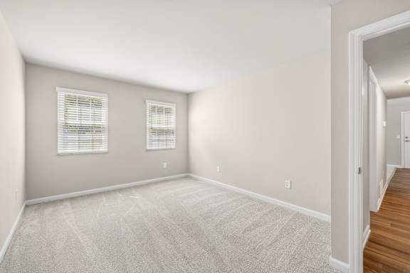 A room with a carpeted floor and two windows with blinds.