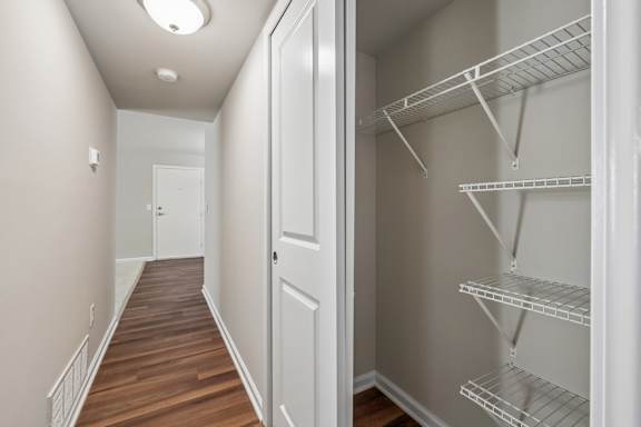 A long hallway with a white door and a white closet with shelves.