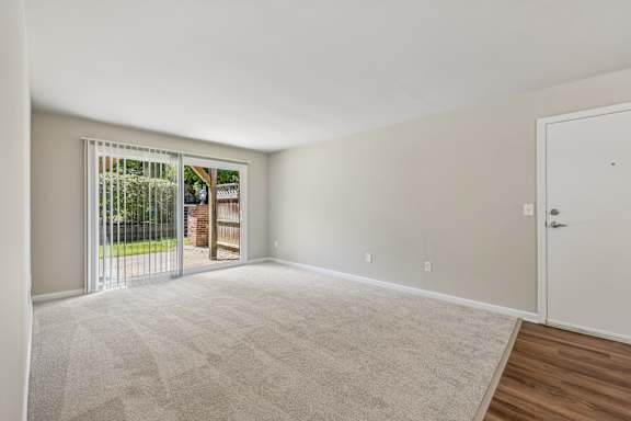 A room with a carpeted floor and a sliding glass door leading to a backyard.