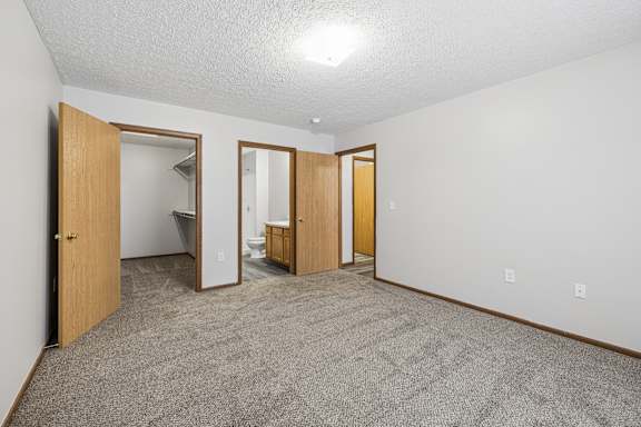 A room with carpeted floor and white walls with a doorway leading to another room.
