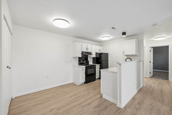 A kitchen with white cabinets and appliances in a room with wooden floors.