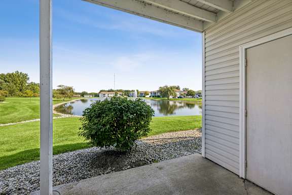 A view from a house looking out to a pond and a green lawn.