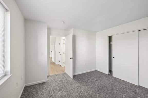 A spacious room with white walls and a grey carpet.