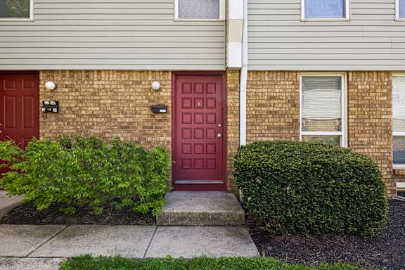 A red door is on the left side of a brick building.