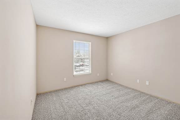 A room with a window showing a view of a house and trees.