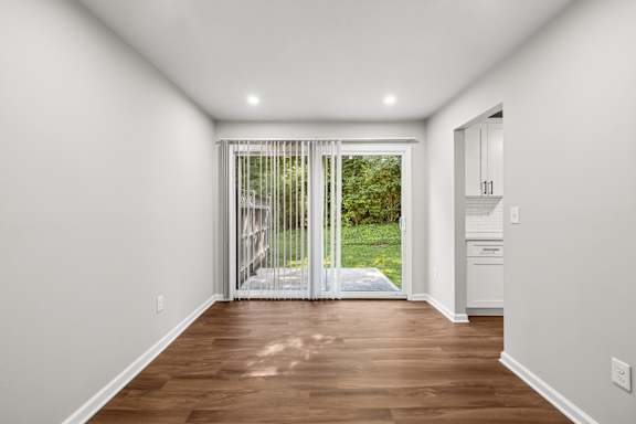 A room with wooden floors and white walls leading to a patio.