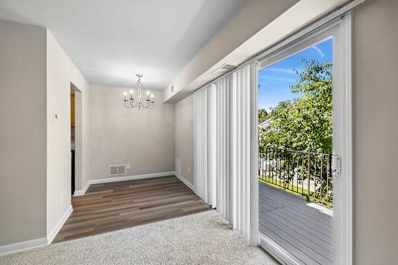A room with a chandelier, sliding glass doors, and a view of a tree-lined street.
