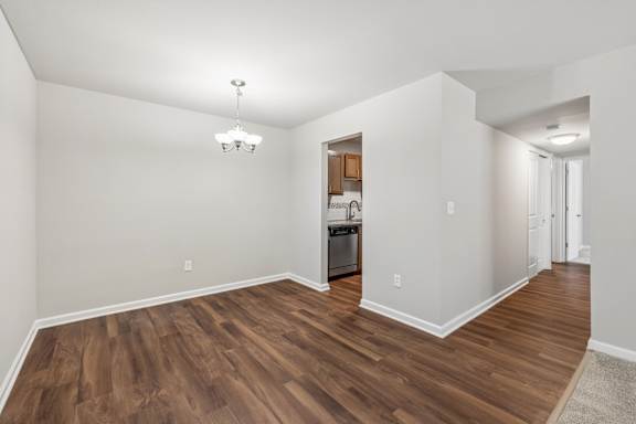 A room with wooden floors and a kitchen area in the background.