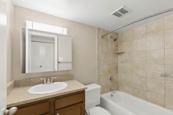 A bathroom with a sink, mirror, toilet, and bathtub.