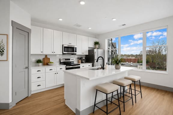 A kitchen with white cabinets and a large island with three stools.