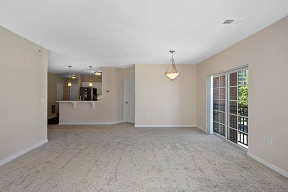 A spacious living room with a carpeted floor and a sliding glass door leading to a balcony. at Roebling Row, Covington, KY, 41011-1720