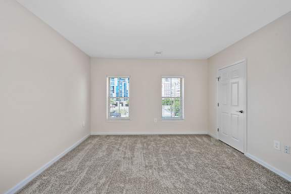 A room with a carpeted floor, two windows with blinds, and a white door. at Roebling Row, Covington, Kentucky