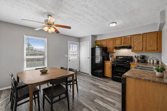 A kitchen with a table and chairs in the foreground and a refrigerator, oven, and microwave in the background.