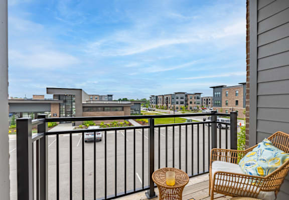 A balcony with a chair and table overlooking a parking lot and buildings.
