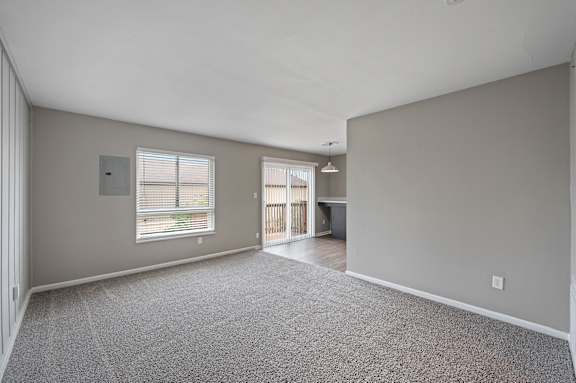 A spacious room with a grey carpet and a window with blinds.