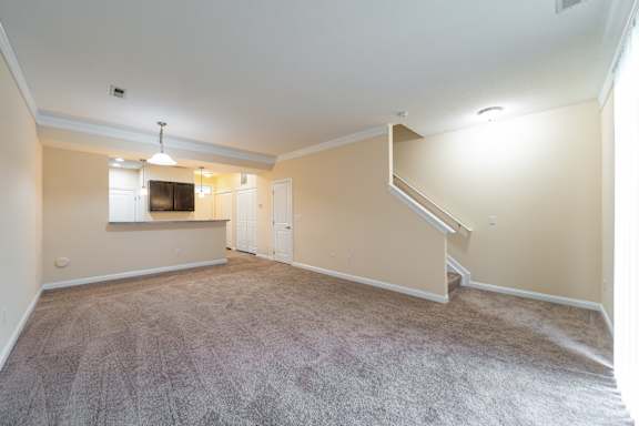 A spacious living room with a carpeted floor and a staircase leading to another room.
