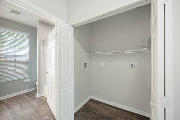 A white door is open to a room with a shelf and a window with blinds.