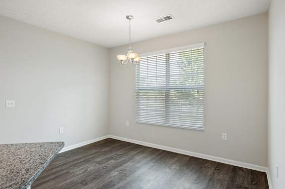 A room with a window covered by blinds and a chandelier hanging from the ceiling.