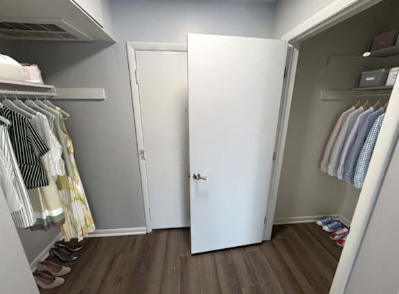 A white closet with clothes hanging and a pair of shoes on the floor.