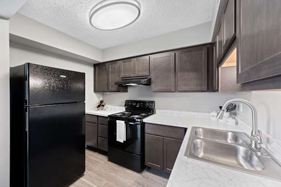 A black fridge and stove in a kitchen with brown cabinets. at The Parkton, Cincinnati, OH, 45231