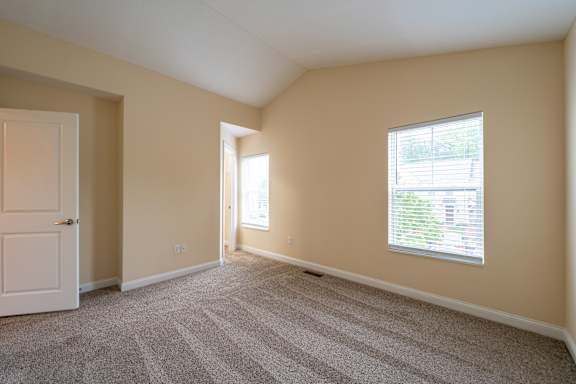 A room with a carpeted floor, a window with blinds, and a door.