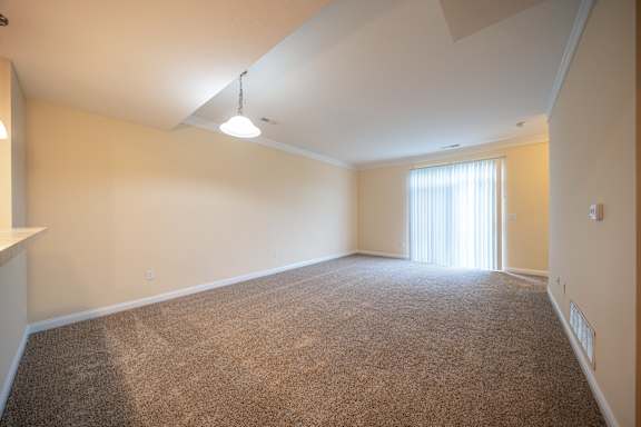 A large, empty room with carpeted floor and a window with blinds.