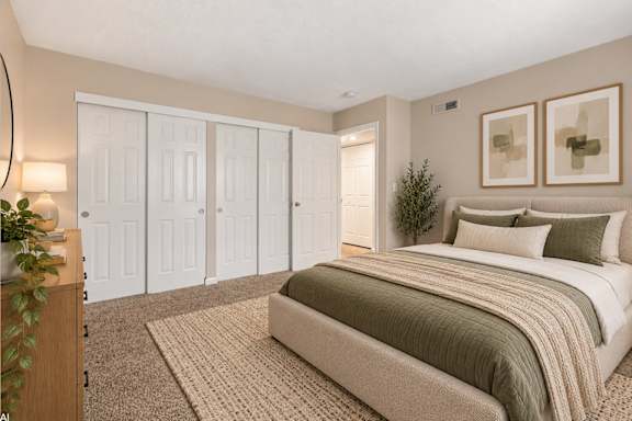 A bedroom with a bed, a plant, and a painting on the wall.
