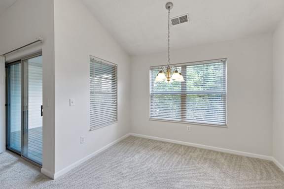 A room with a carpeted floor, a window with blinds, and a hanging light fixture.