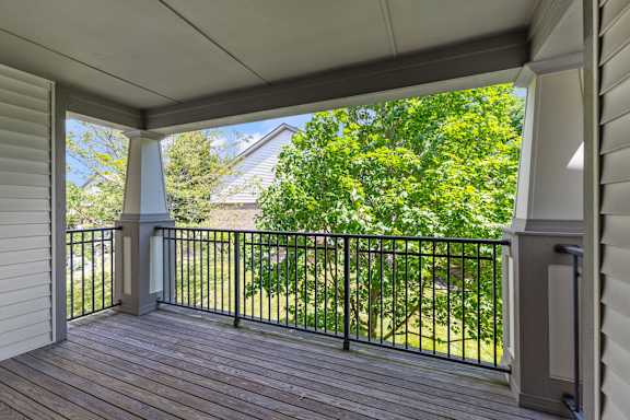 A balcony with a black railing and a view of a green lawn and trees.