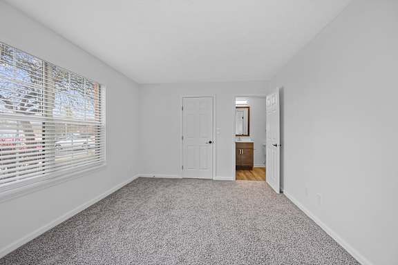 A room with a carpeted floor and a window with blinds at Indian Lookout Apartments, West Carrollton, OH, 45449